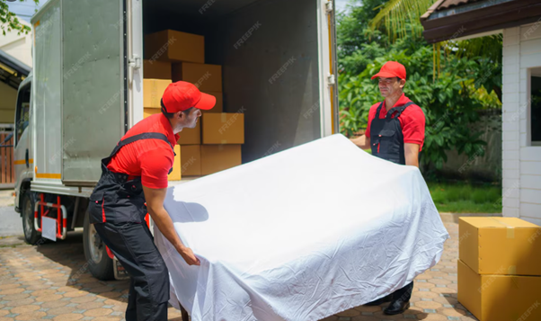 Two men loading a white covered sofa into a moving truck